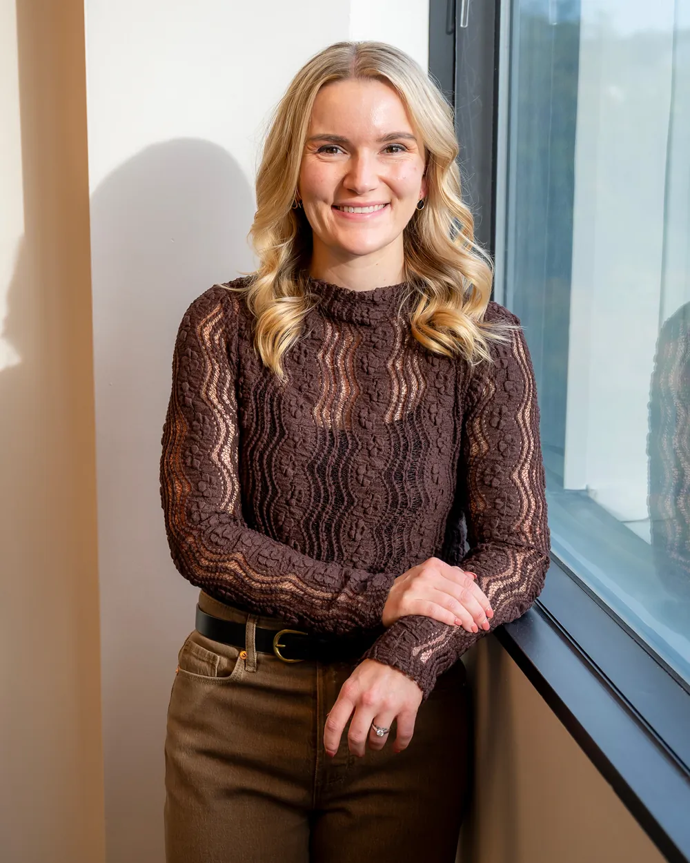 Dr. Kate smiling, leaning beside a sunlit office window